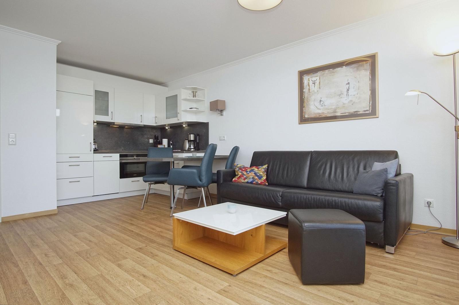 Living area with sofa, coffee table, and integrated kitchen.