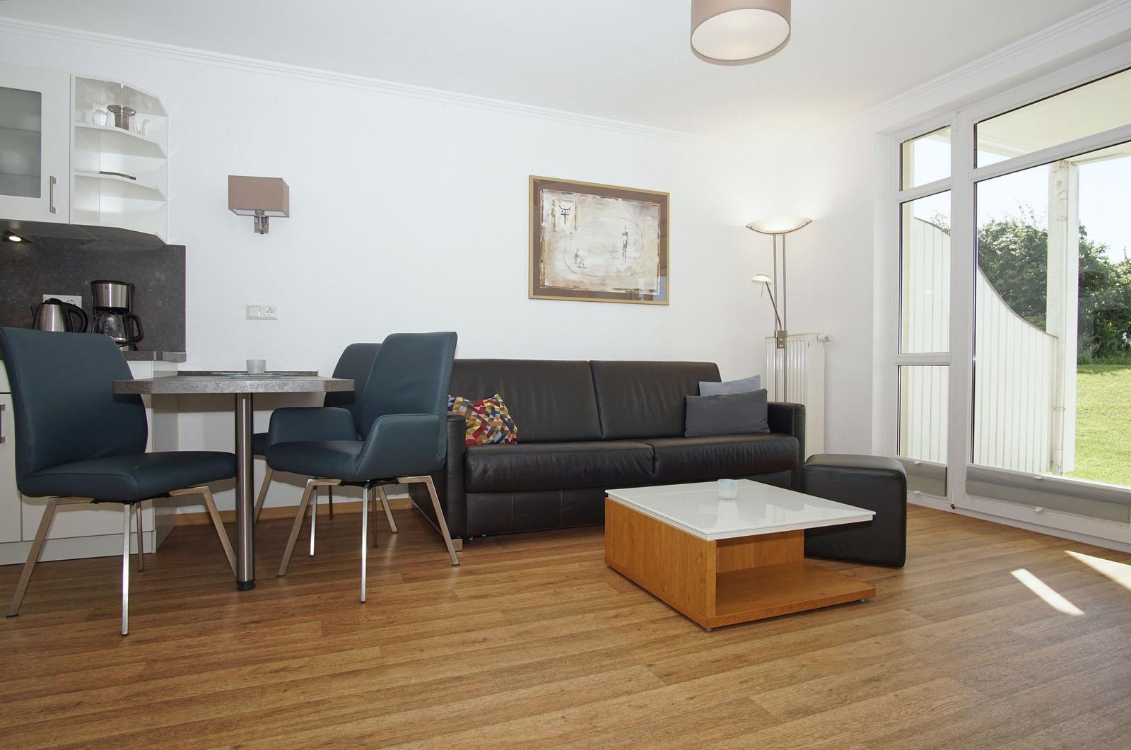 Living and dining area with sofa, table and chairs. Large glass doors lead to a terrace.