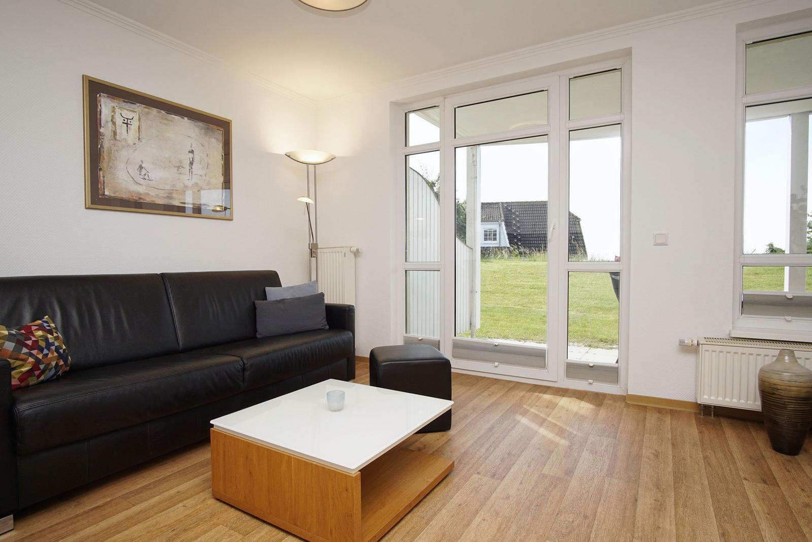 Living room with sofa, coffee table, and large window overlooking green outdoor area.