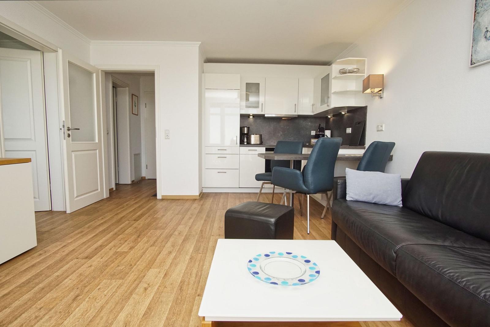 Wohnzimmer mit Sofa, Esstisch und Küche im Hintergrund.