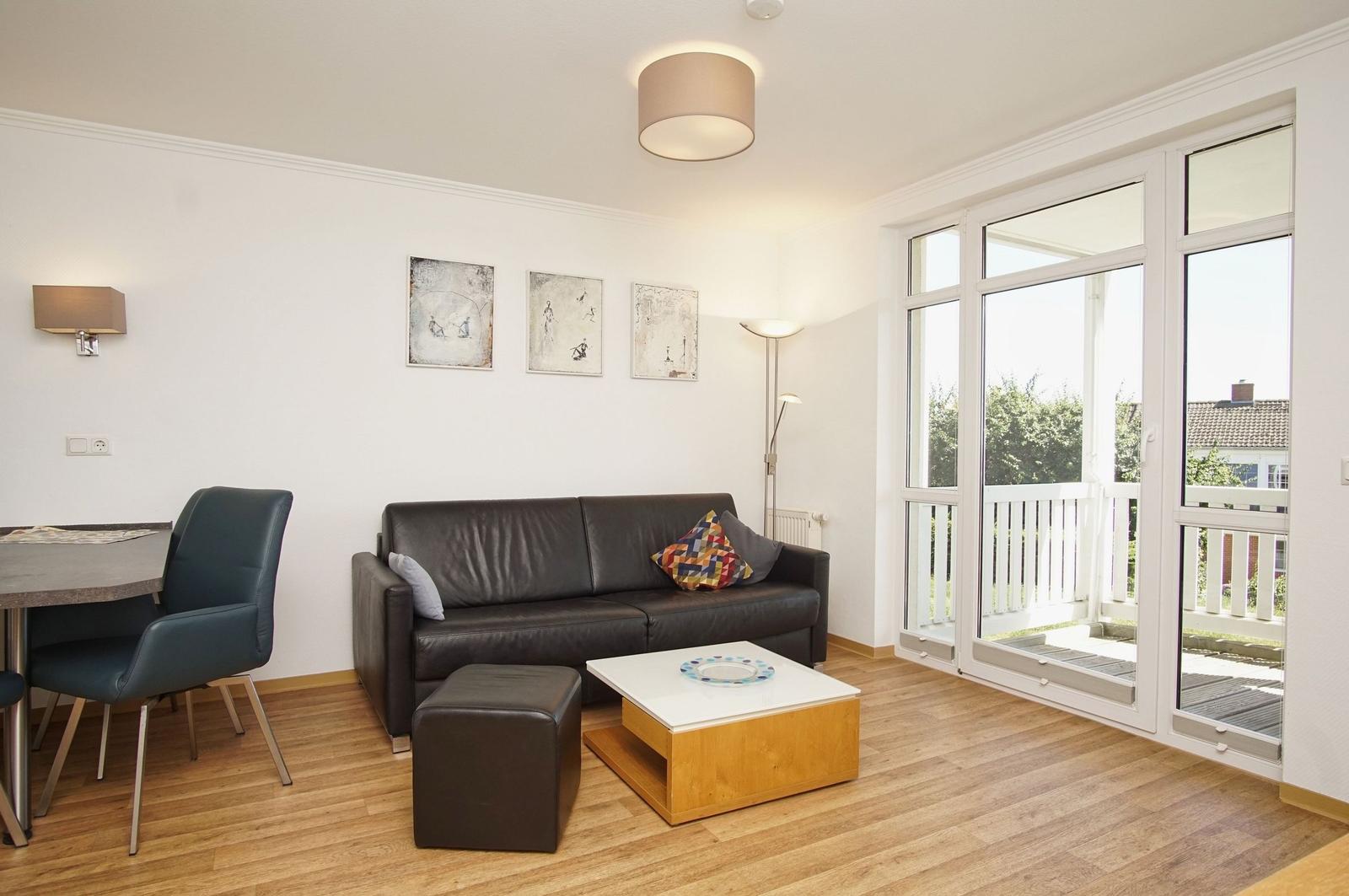 Wohnzimmer mit Sofa, Tisch und Balkon. Holzboden und große Fenster.