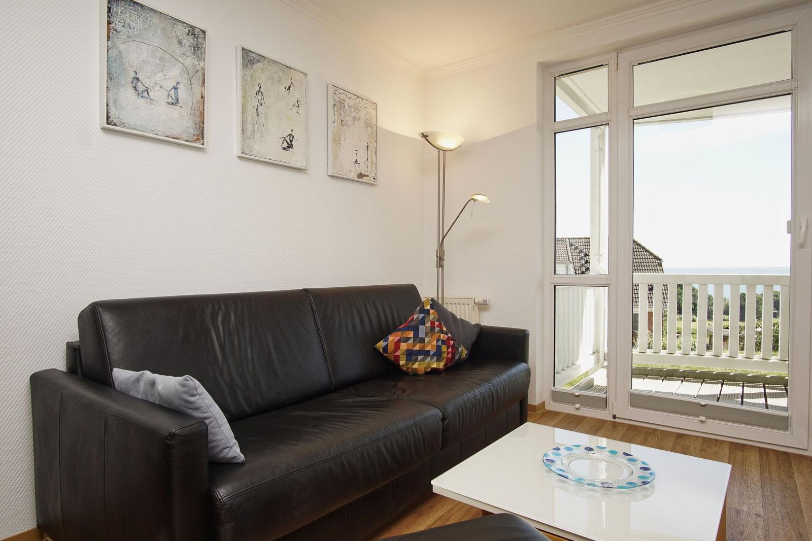 Schwarzes Sofa mit Kissen, weiße Couchtisch und Fenster zur Terrasse.