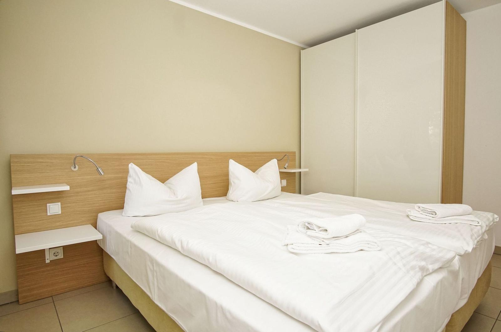 Ein Bett mit weißen Laken und Kissen. An der Wand hängen zwei Lampen und ein Schrank.