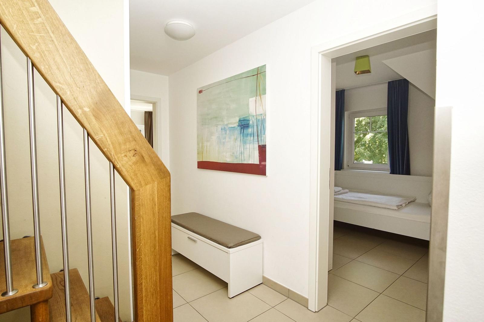 Flur mit Holzgeländer, Wandbild und Blick in Schlafzimmer mit Fenster und Bett.