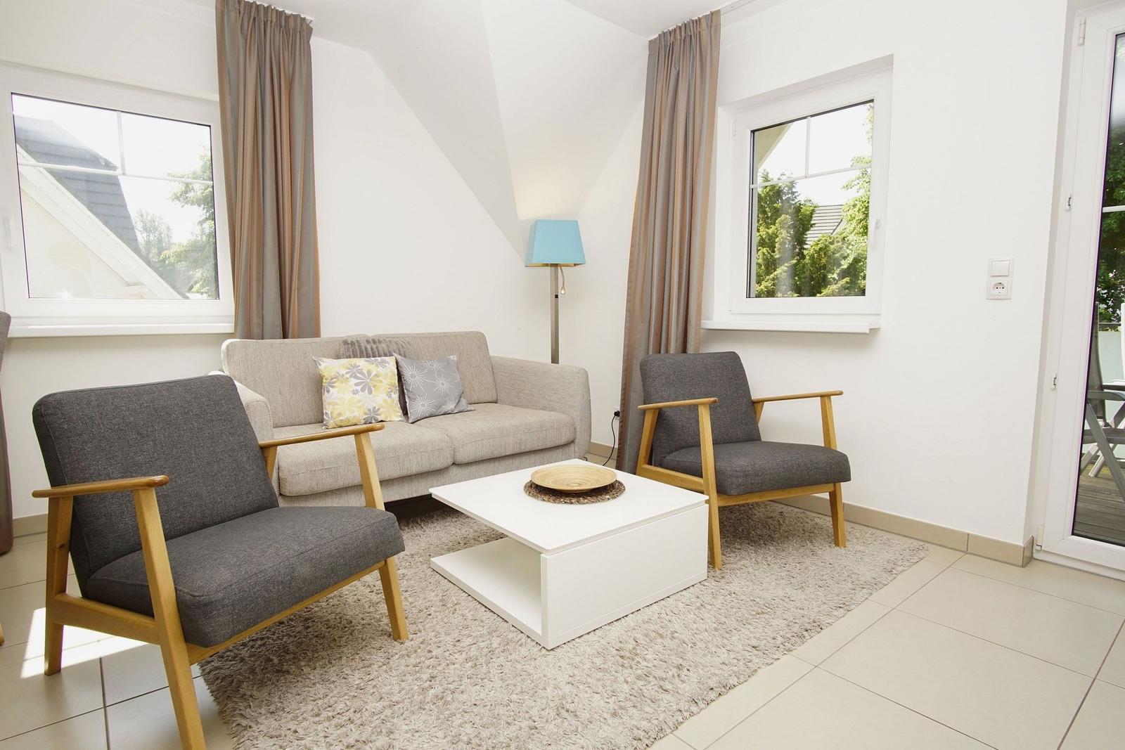 Wohnzimmer mit Sofa, zwei Sesseln, Tisch und Fenstern.