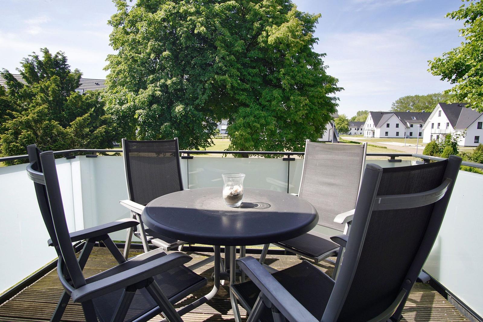 Terrasse mit runden Tisch und vier Stühlen, Blick auf Bäume und Häuser.