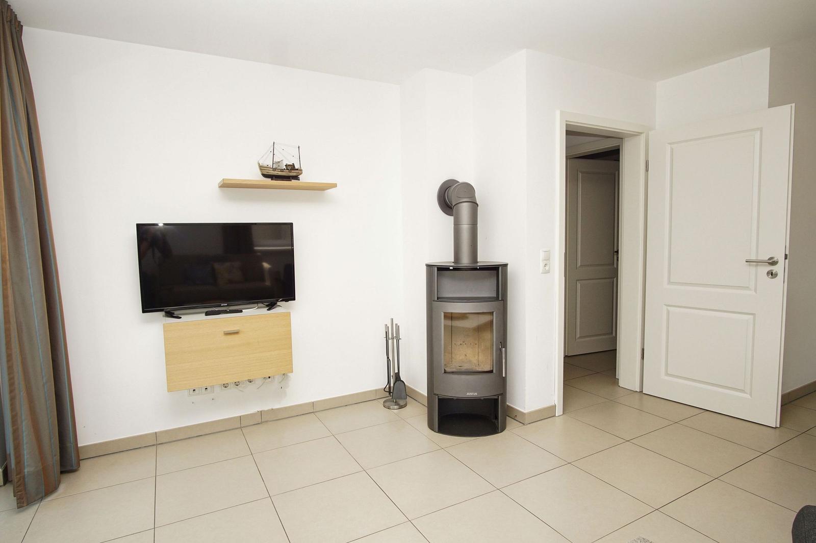 Wohnzimmer mit Fernseher, Kaminofen und Tür zu anderen Räumen.