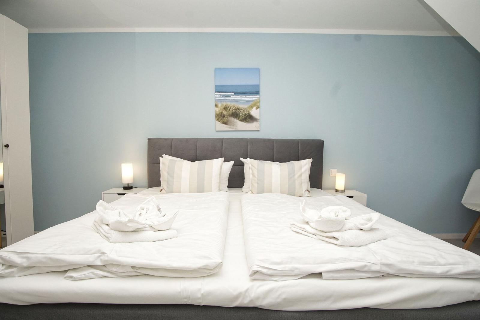 Doppelbett mit weißer Bettwäsche und Strandbild an der Wand.