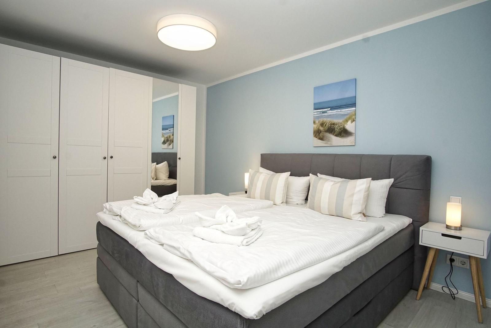Schlafzimmer mit Doppelbett, weißen Bettwäsche und Strandbild an der Wand.