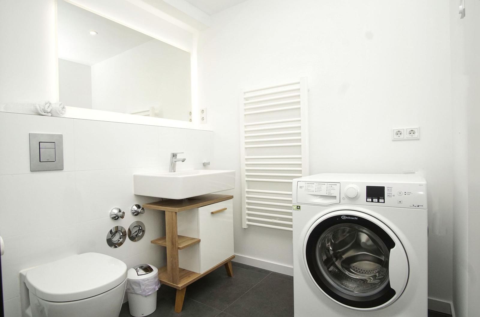 Badezimmer mit Waschmaschine, Spülung, Waschtisch und Heizkörper.