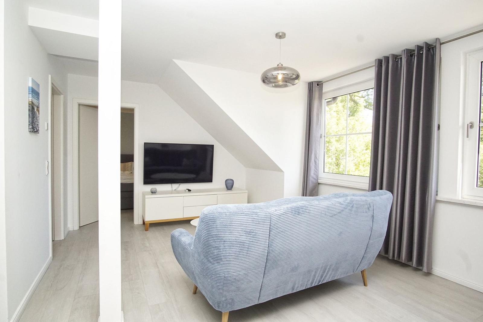 Wohnzimmer mit Sofa, TV und Fenster mit Vorhängen.