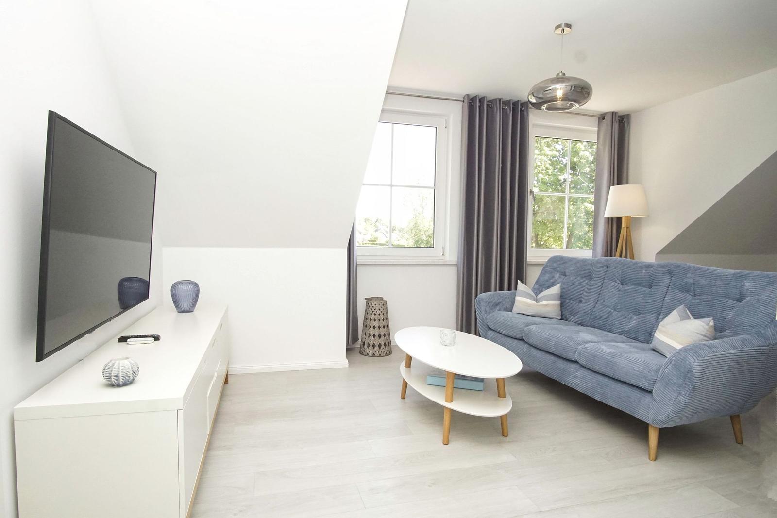 Wohnzimmer mit blauem Sofa, weißem Couchtisch und Fernseher an der Wand.