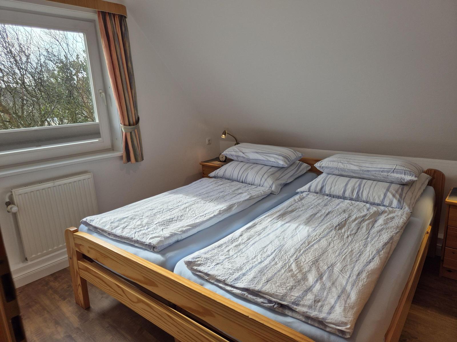 Zwei Einzelbetten mit Bettwäsche, Fenster mit Vorhängen und Nachttisch mit Lampe.