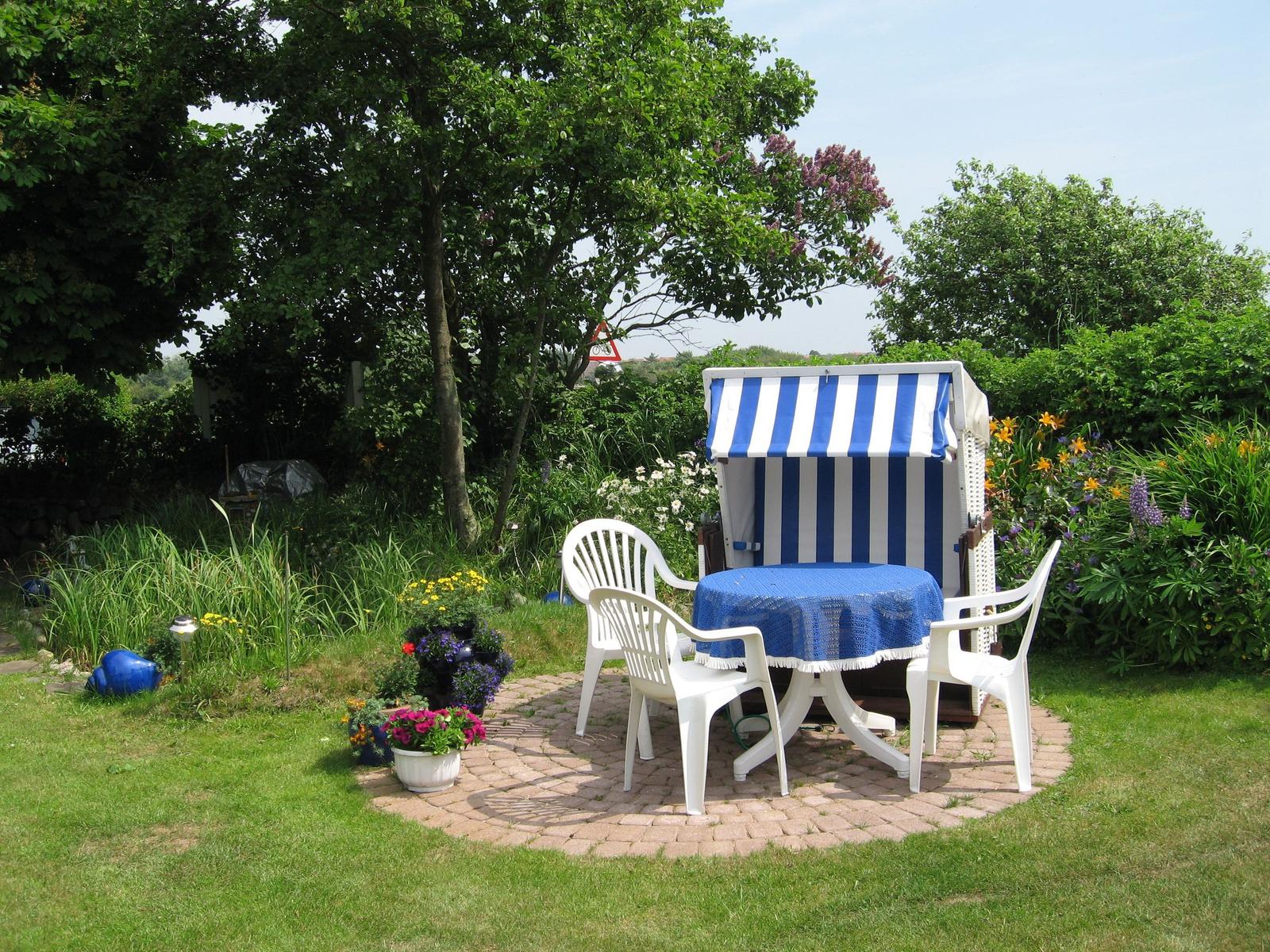 Garten mit Strandkorb, Tisch und Stühlen, Blumen und Bäumen umgeben.