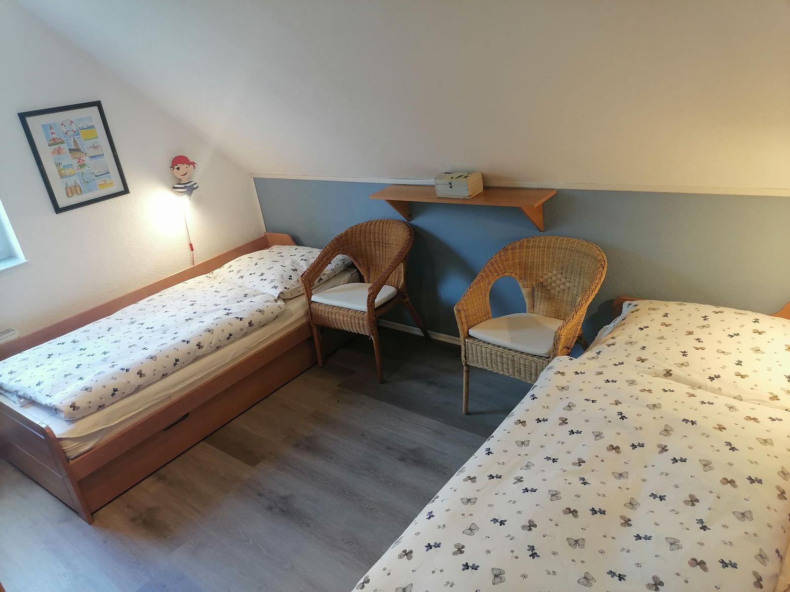 Zimmer mit zwei Betten, zwei Stühlen und Wandregal. Dachschräge und Fenster sichtbar.