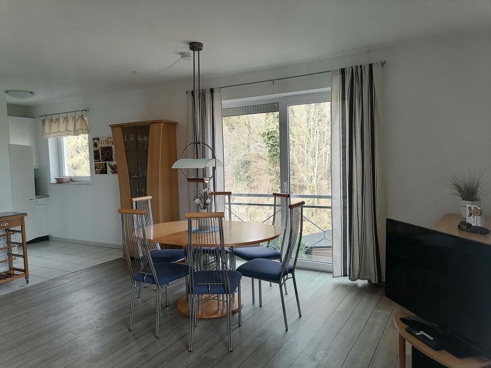 Essbereich mit Tisch, Stühlen und Balkontür. Küche und Wohnbereich sichtbar.