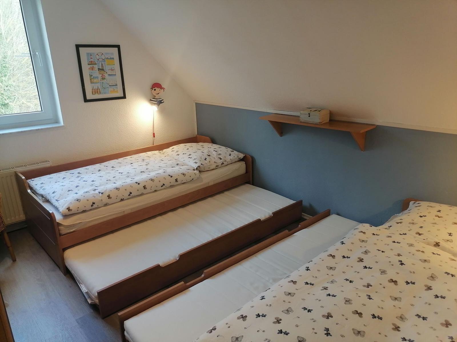 Schlafzimmer mit Doppelbett und zwei ausziehbaren Matratzen. Wand mit Schreibtisch und Bild.