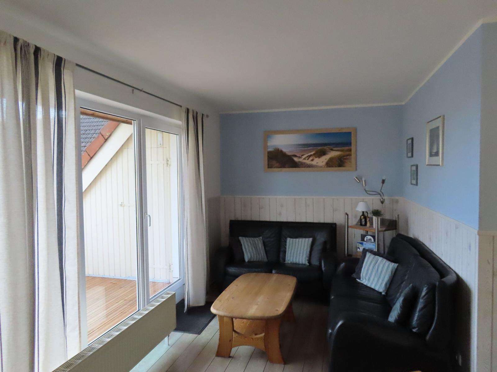 Wohnzimmer mit zwei schwarzen Sofas, Holztisch und Fenster zur Terrasse.