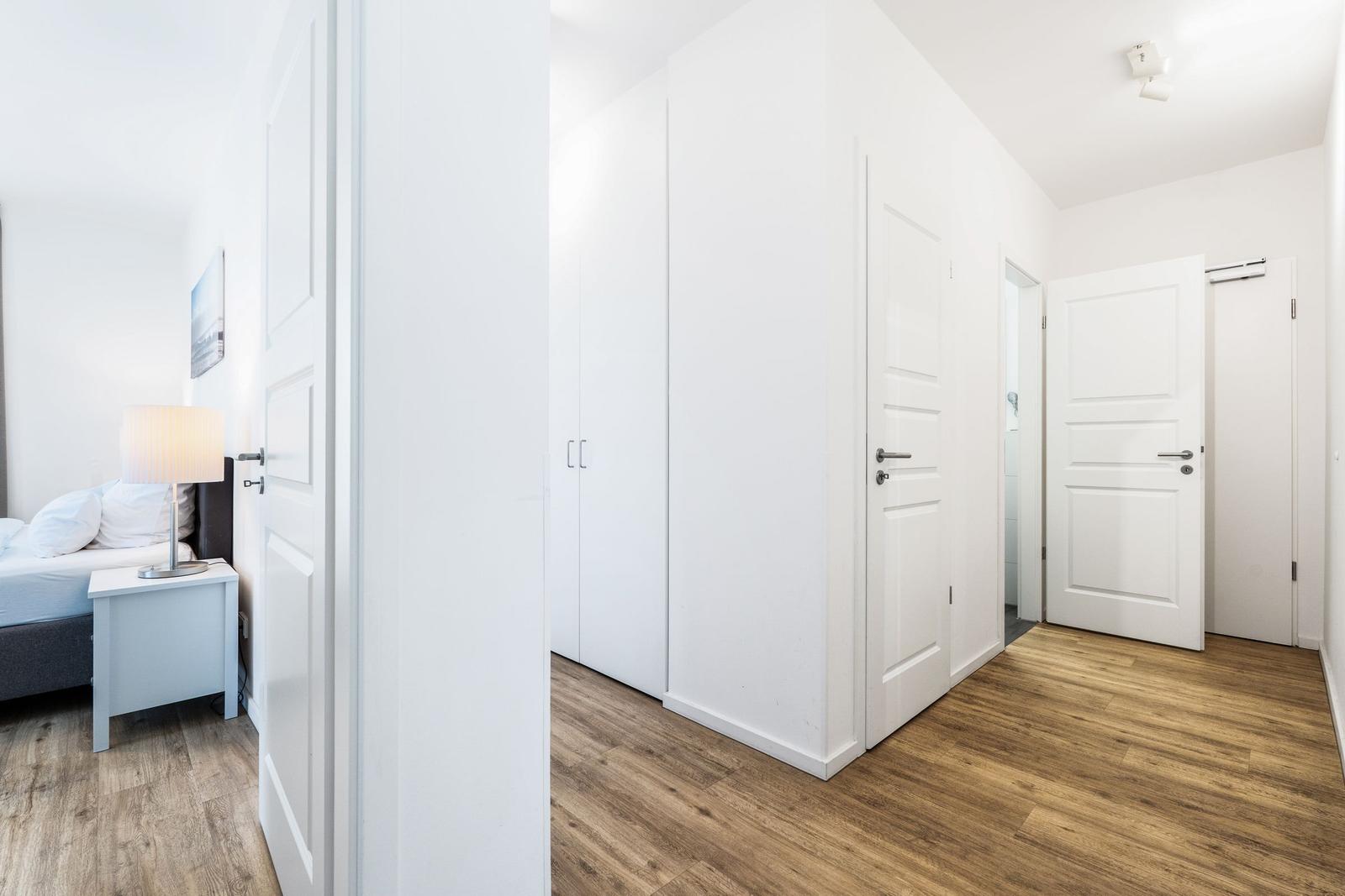 Schlafzimmer mit Bett und Nachttisch. Flur mit Schrank und Türen. Holzfußboden.