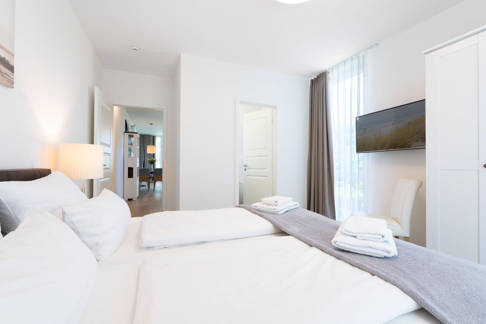Schlafzimmer mit Bett, TV und Blick in Wohnbereich.
