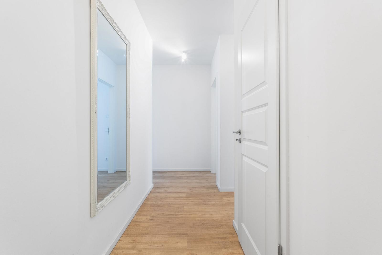 Flur mit Holzboden, Spiegel an der Wand und weißen Türen.