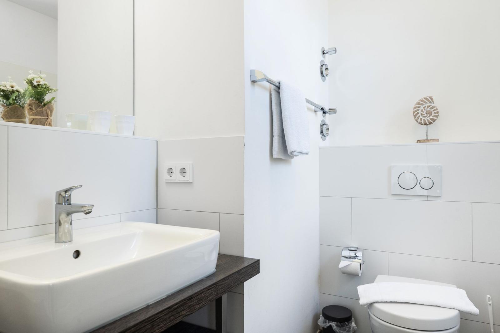 Badezimmer mit Waschbecken, Spiegel, Toilette und Handtuchhalter.
