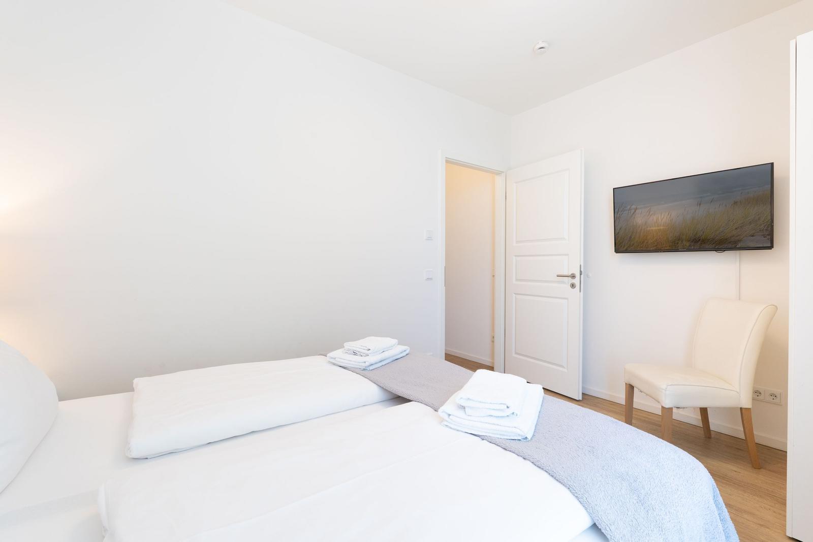 Schlafzimmer mit Bett, Handtuch und Stuhl. Wandbild und Tür sichtbar.
