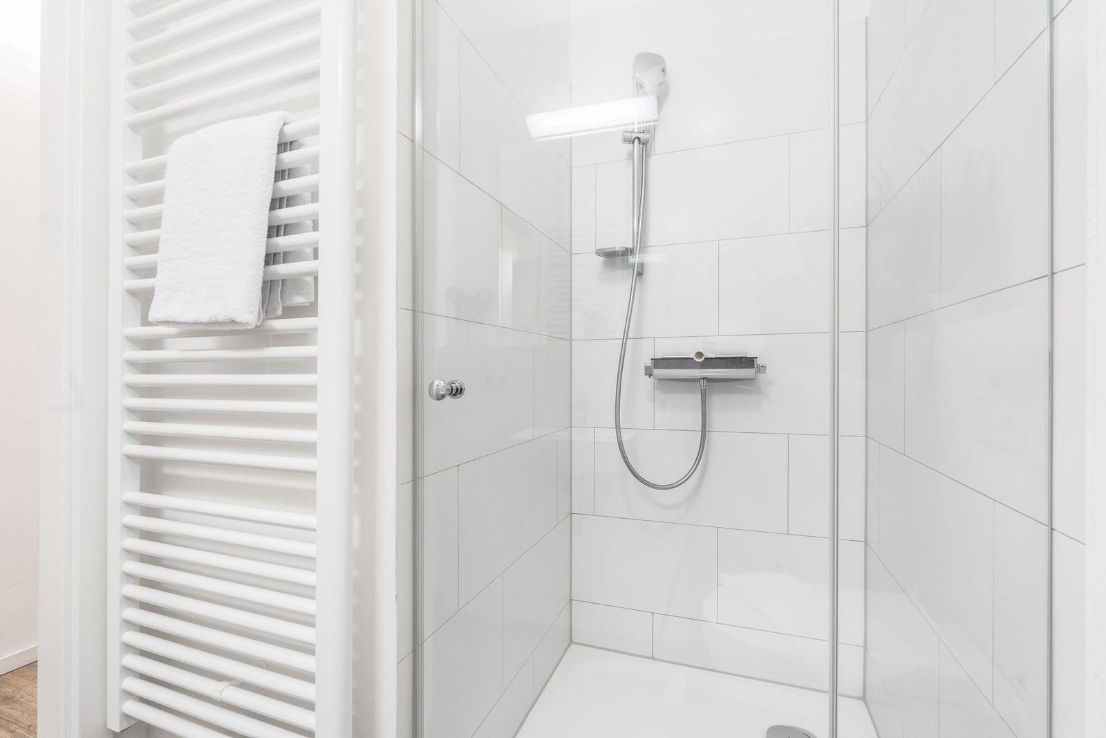 Dusche mit Glaswand und Heizkörper mit Handtuch.