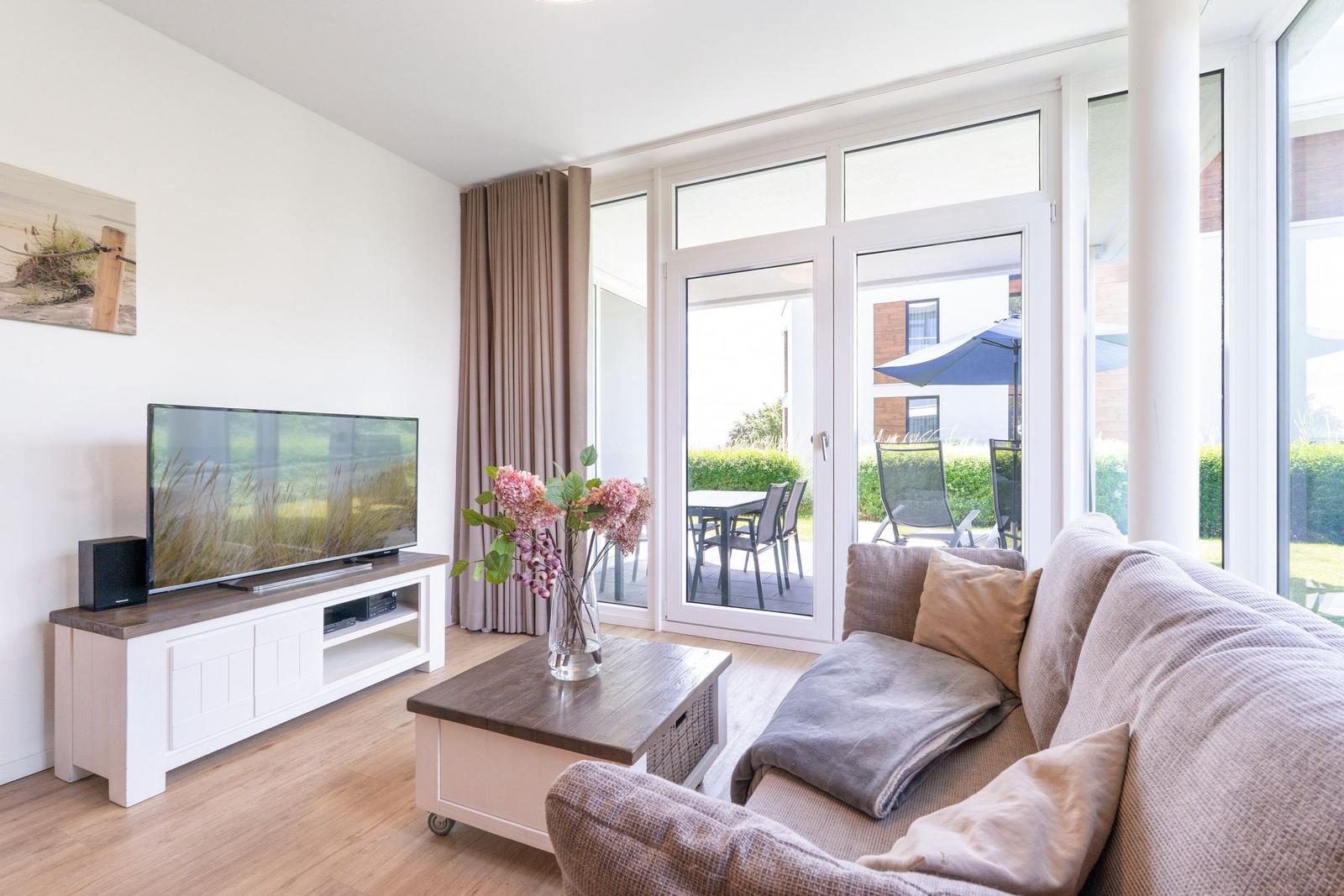Wohnzimmer mit Sofa, Fernseher und Blick auf die Terrasse.