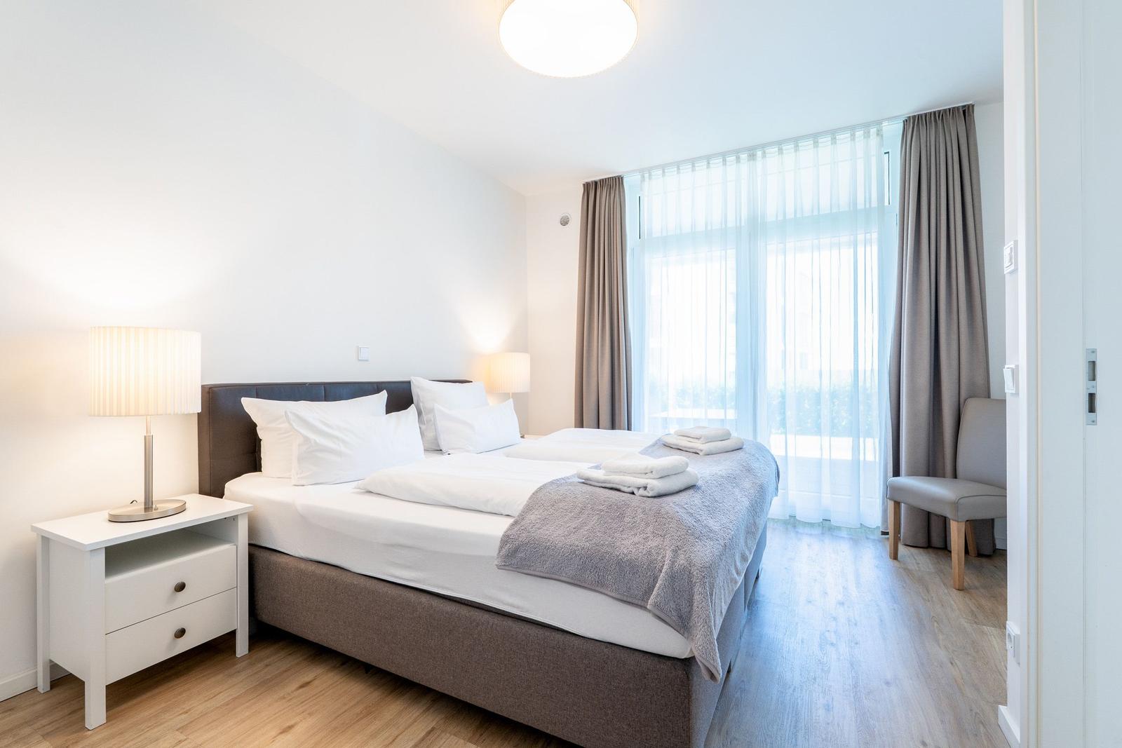 Schlafzimmer mit Doppelbett, Nachttisch und Fenster mit Vorhängen.