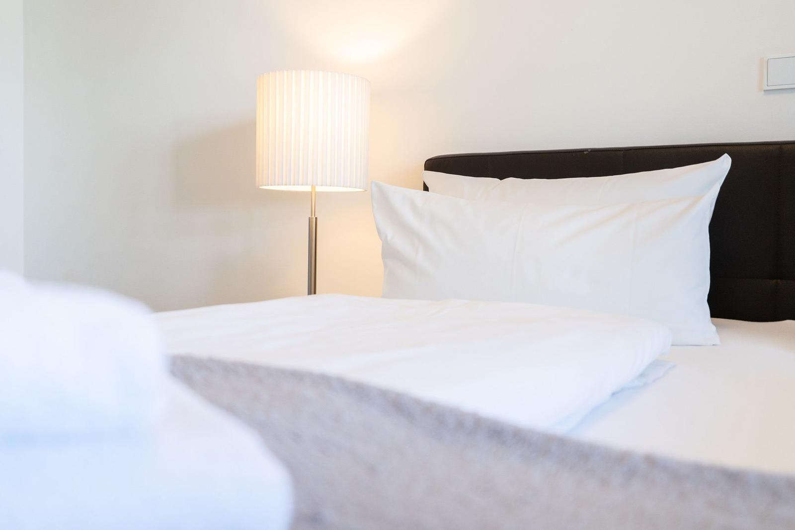 Das Bett mit weißen Kissen und einer Stehlampe an der Wand.
