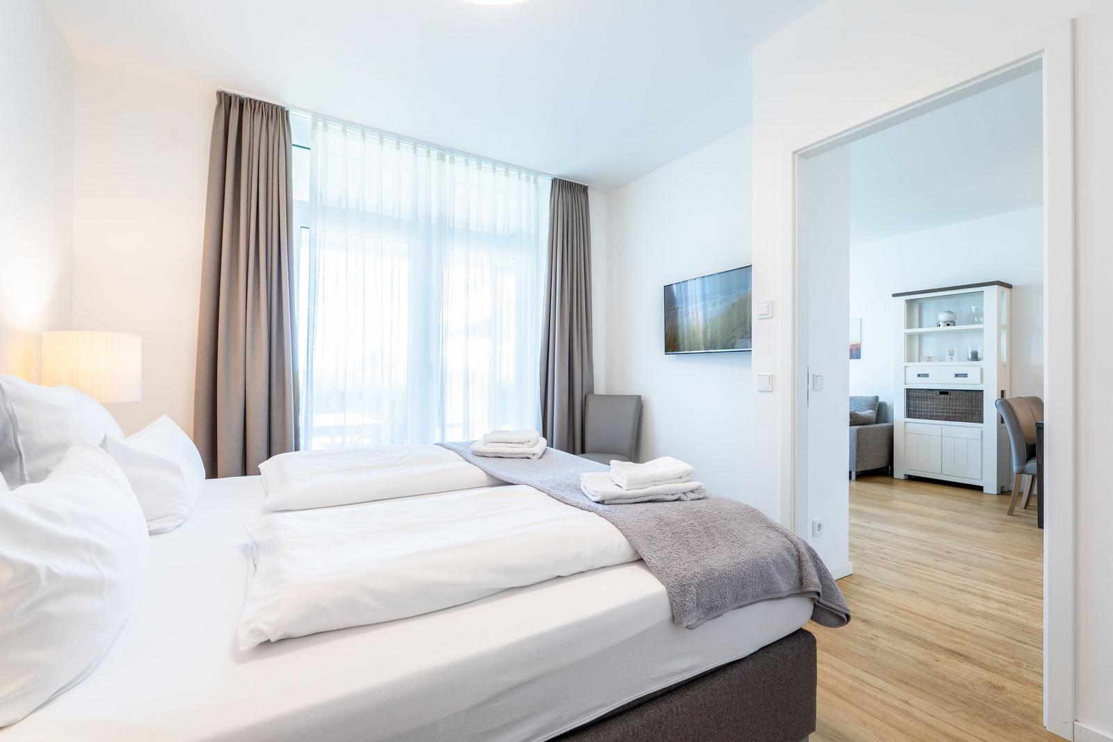 Ein Schlafzimmer mit einem Bett, einem Fenster und einem Zugang zum Wohnbereich.