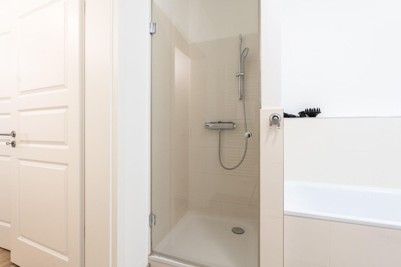 Dusche mit Glaswand und Badewanne in weißer Umgebung.