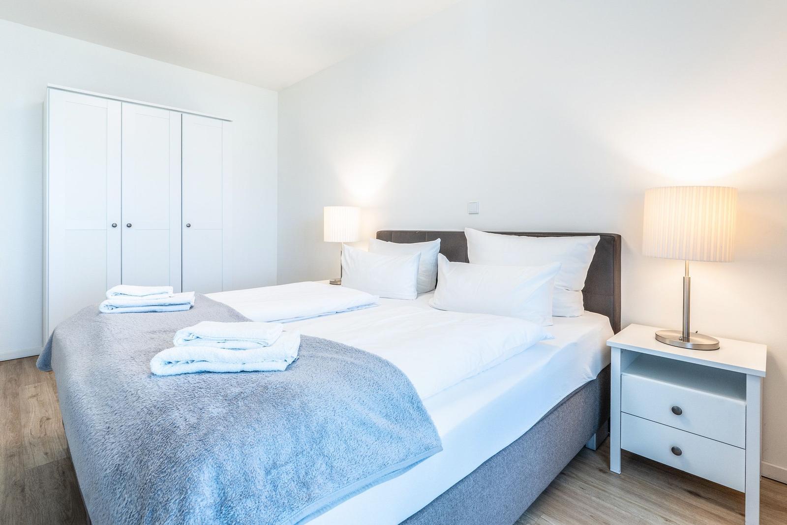 Schlafzimmer mit Bett, Nachttisch und Kleiderschrank. Auf dem Bett liegen Handtücher.
