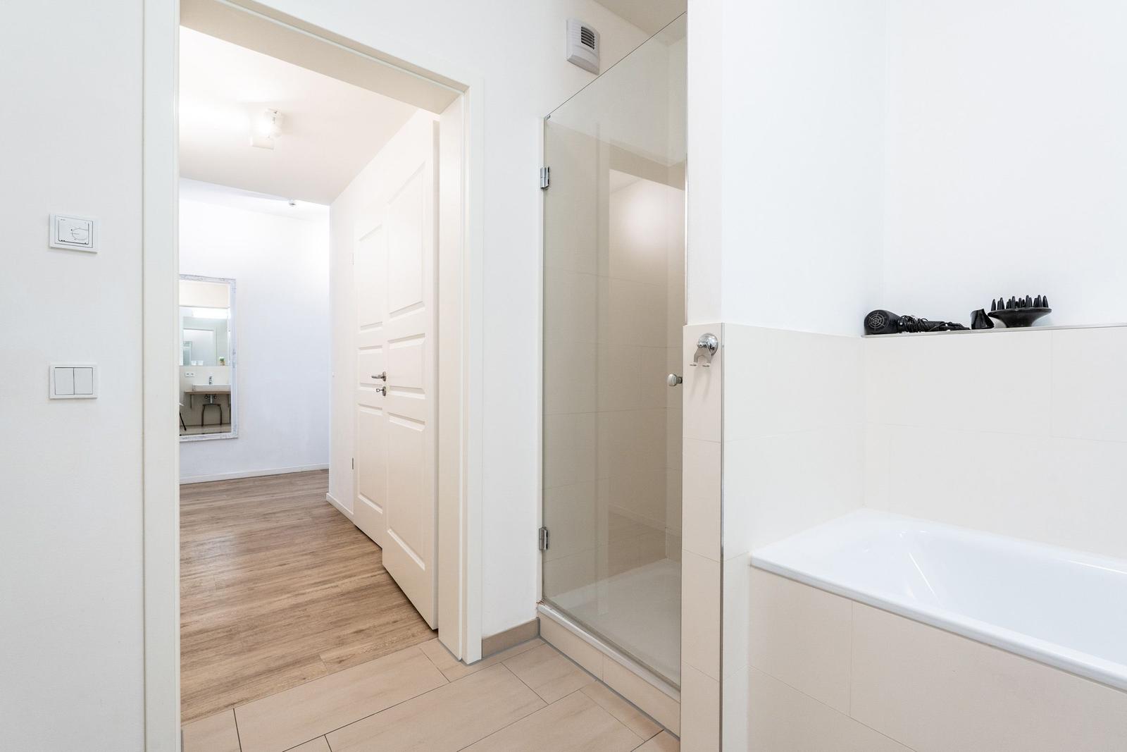 Badezimmer mit Dusche und Badewanne. Durchgang zur angrenzenden Wohnung.
