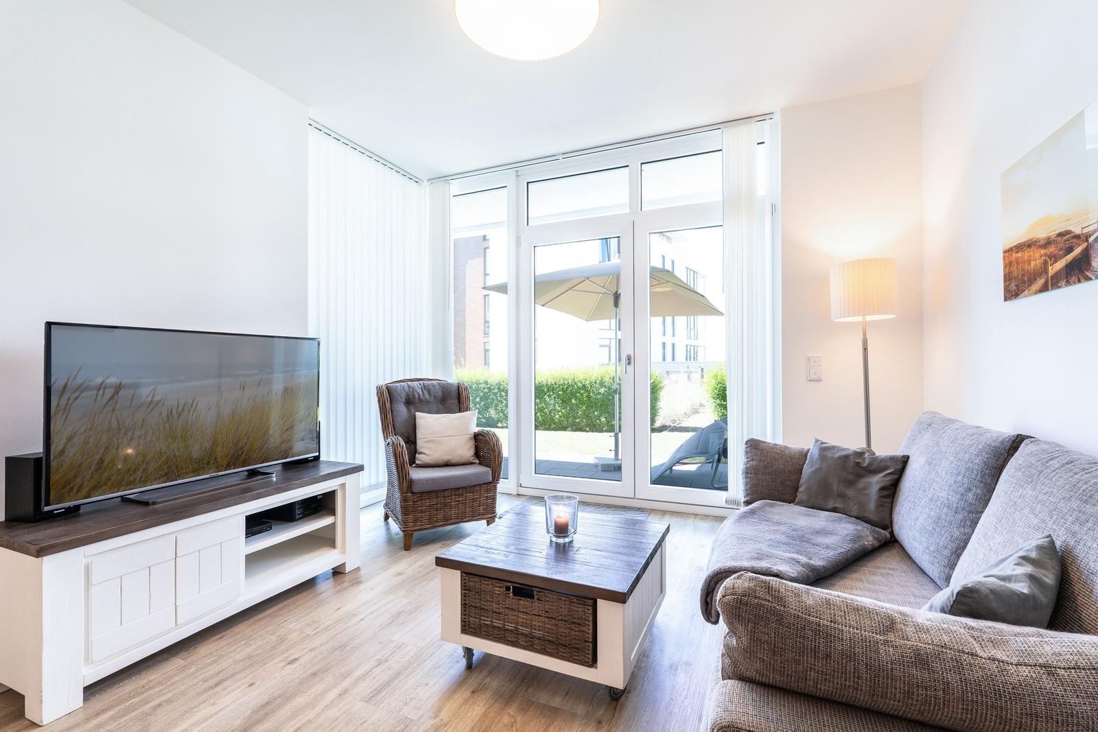 Wohnzimmer mit Sofa, Sessel, Fernseher und Terrassentür.