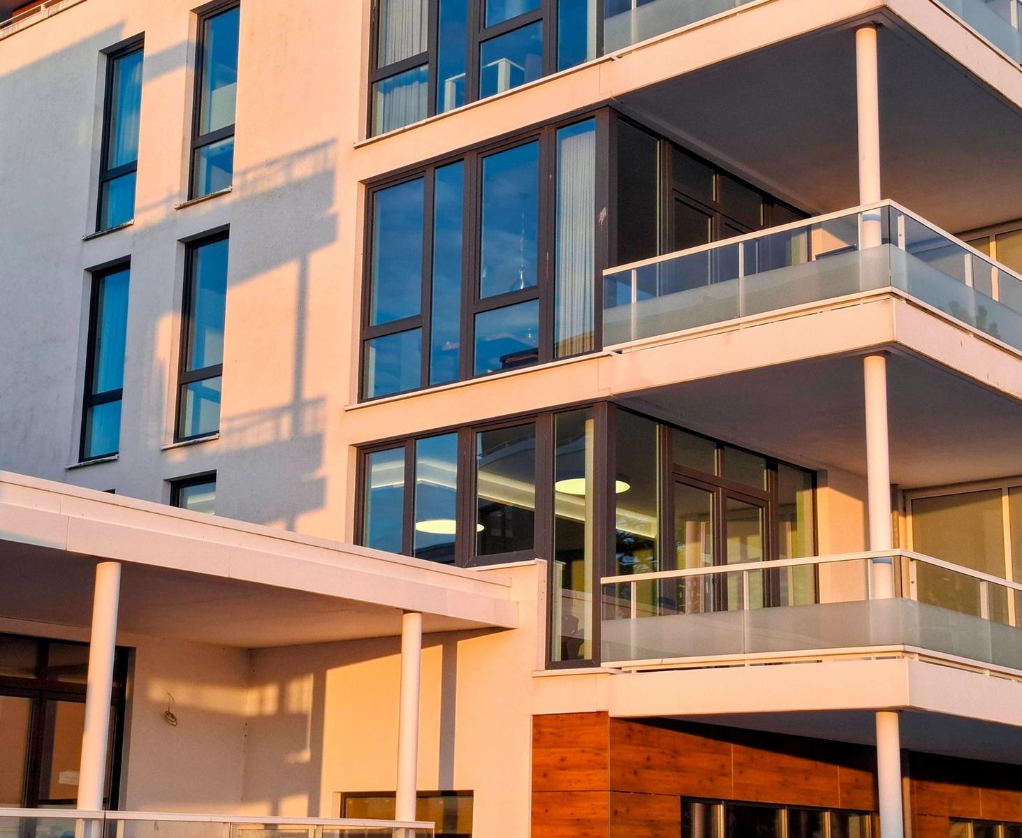 Modernes Gebäude mit großen Fenstern und Balkonen. Sonnenlicht fällt auf die Fassade.