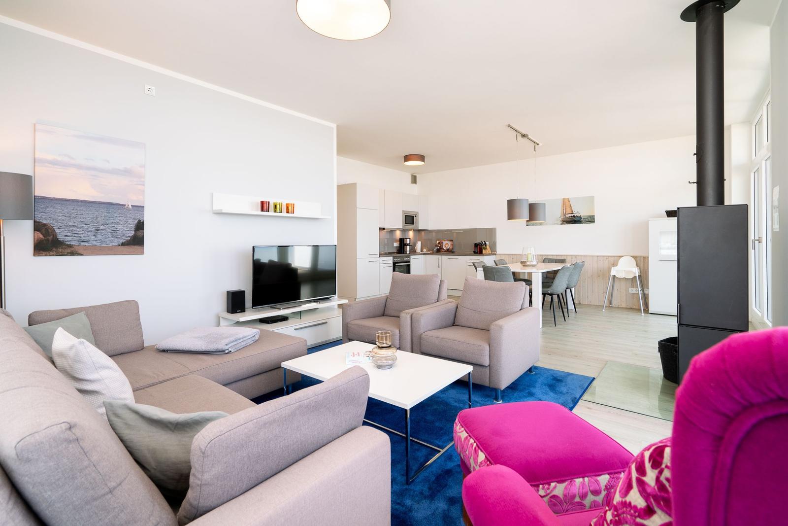 Wohnbereich mit Sofa, Sesseln und Küchenbereich im Hintergrund.
