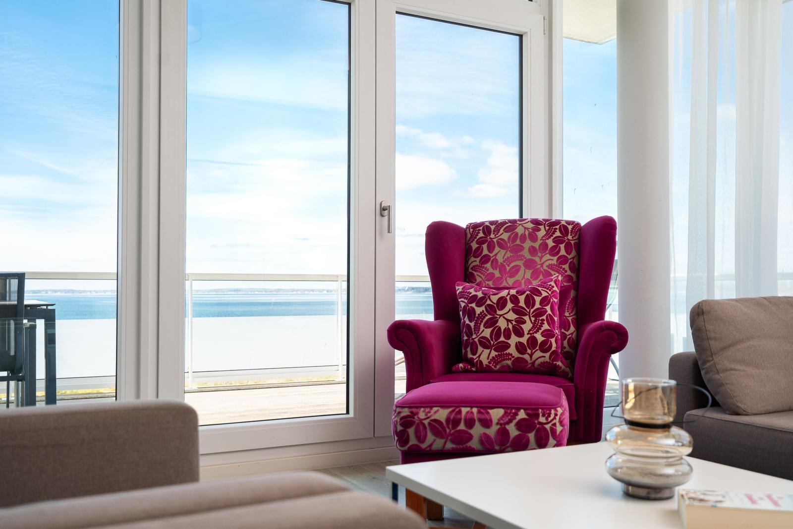 Ein roter Sessel mit Muster steht vor großem Fenster mit Meerblick.