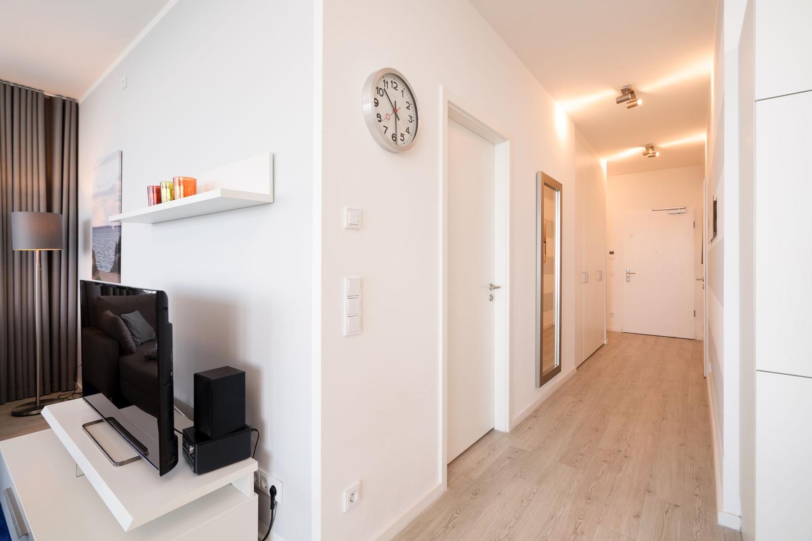 Wohnbereich mit Fernseher und Flur mit Uhr und Spiegel.
