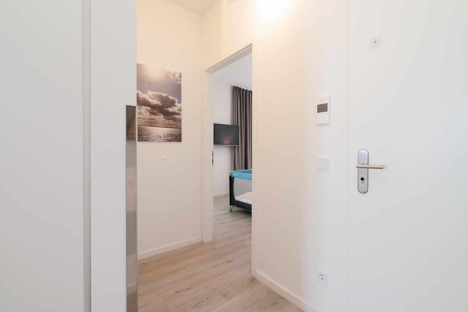 Eingangsbereich mit Blick in Schlafzimmer. Wandbild, Tür und Bodenbelag sichtbar.