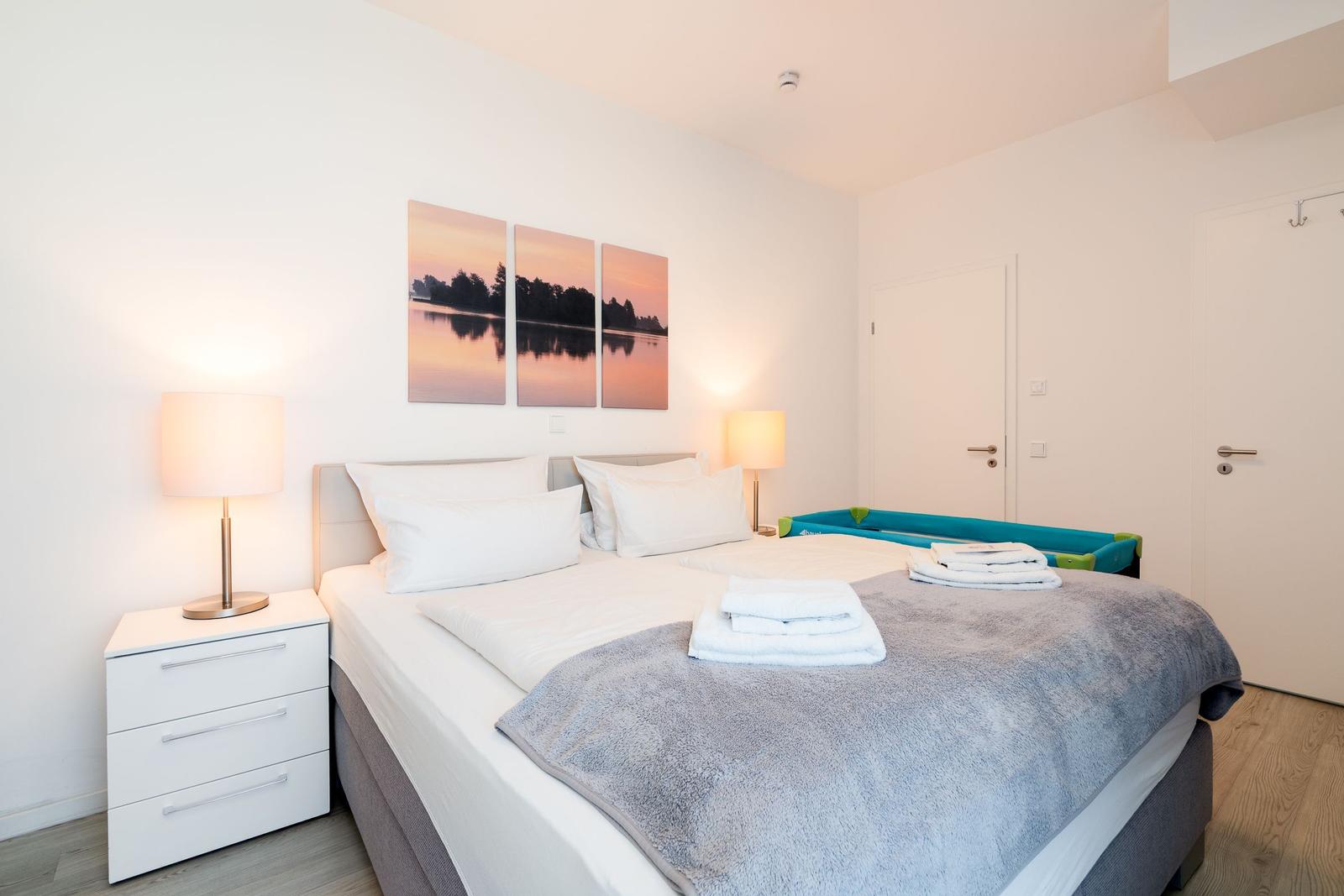 Schlafzimmer mit Doppelbett, Nachttisch und Wandbild. Auf dem Bett liegen Handtücher.