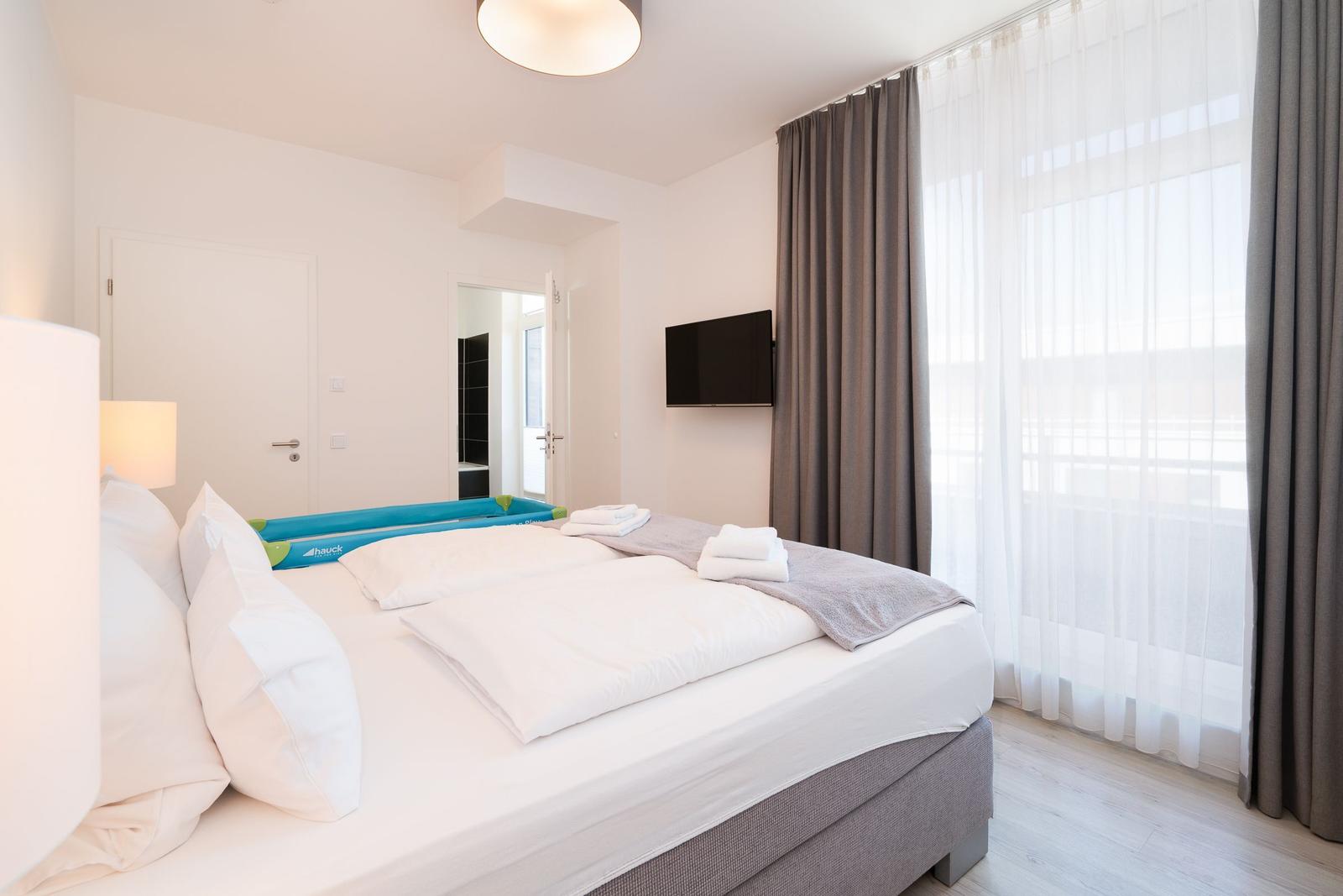 Schlafzimmer mit Bett, TV und Fenster mit Vorhängen.