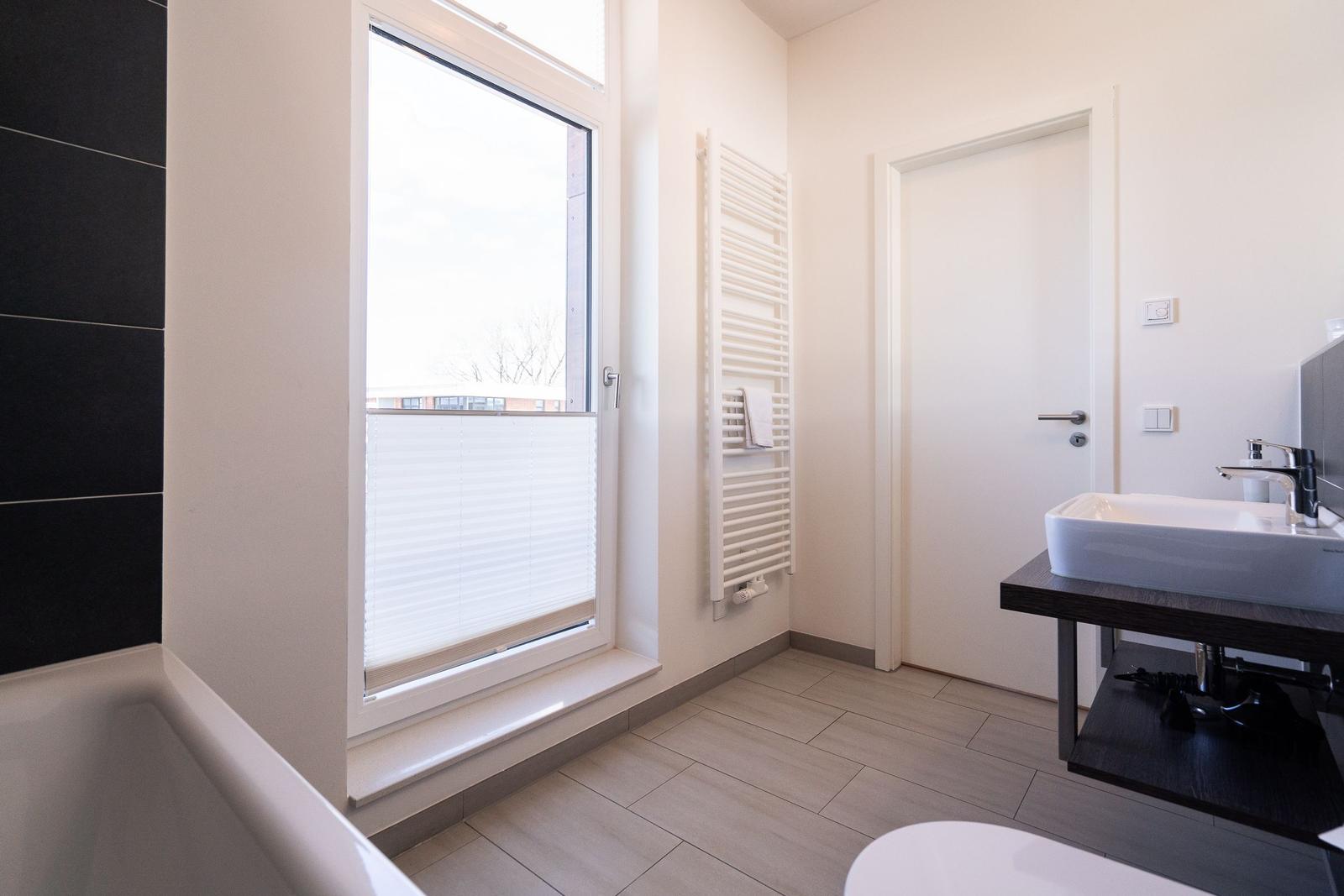 Badezimmer mit Fenster, Handtuchhalter, Waschbecken und Dusche.