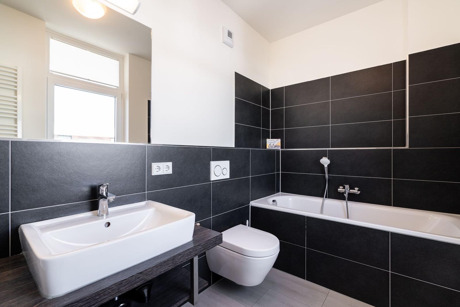 Badezimmer mit Dusche, Waschbecken und Toilette. Schwarze Fliesen an den Wänden.