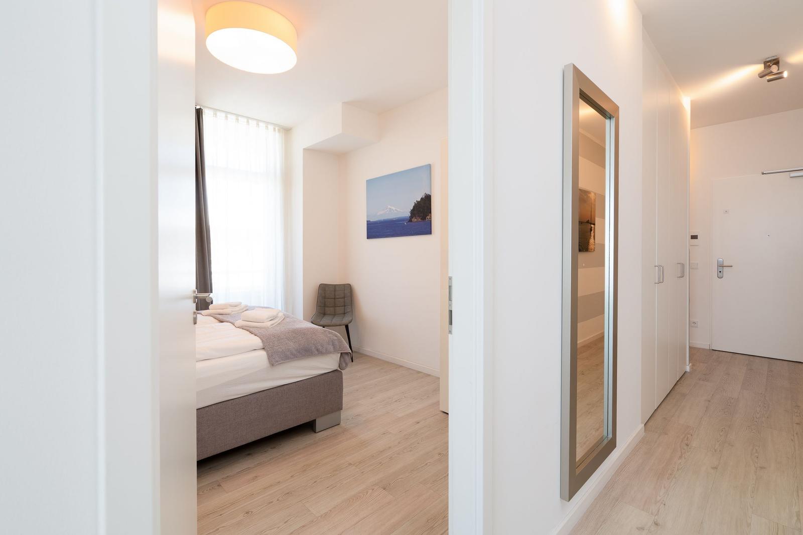 Schlafzimmer mit Bett, Stuhl und Wandbild. Flur mit Spiegel und Schrank.