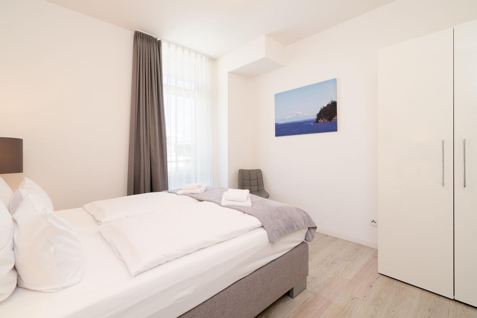 Schlafzimmer mit Bett, Kleiderschrank und Fenster mit Vorhängen.