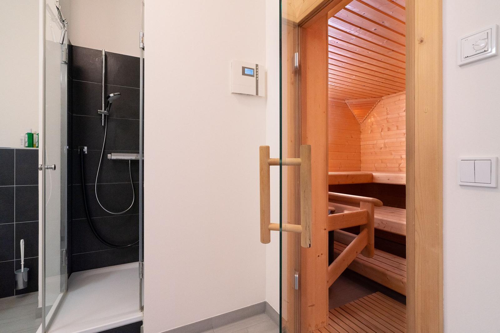 Dusche mit Glaswand und Sauna mit Holzbänken und -decke.
