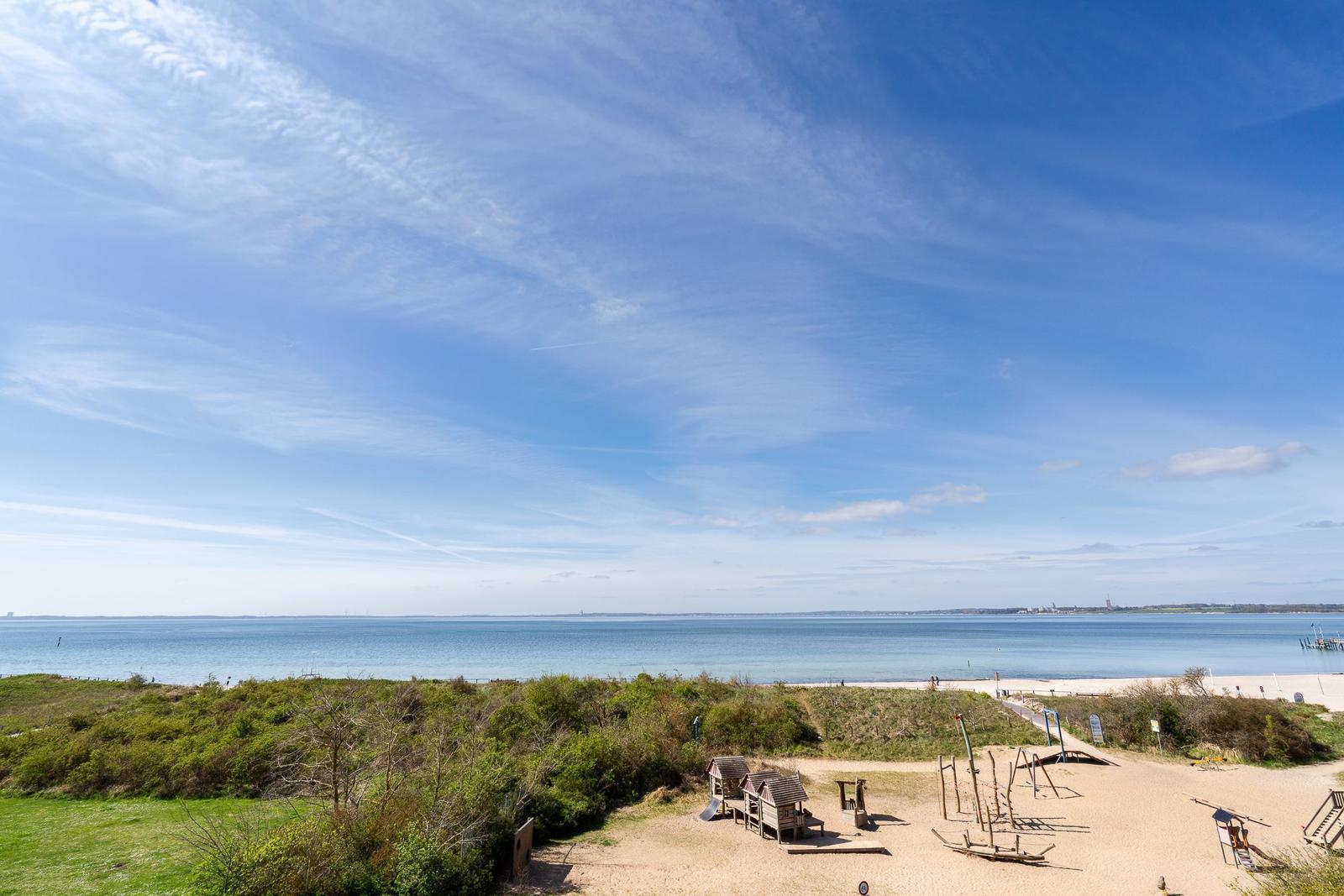 Strandufer mit Spielplatz und Blick auf das Meer unter blauem Himmel.