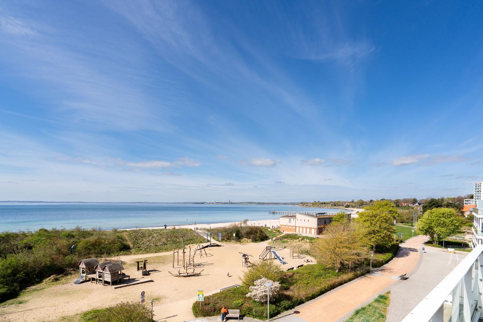 Panoramablick auf Strand, Spielplatz und Küstenstraße unter blauem Himmel.